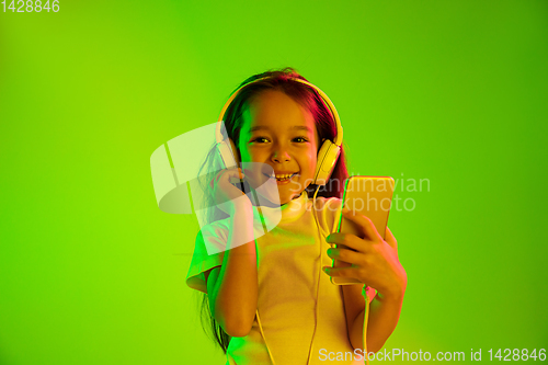 Image of Portrait of little girl in headphones on green background in neon light