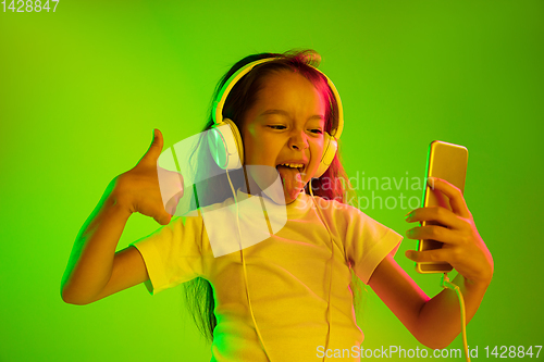 Image of Portrait of little girl in headphones on green background in neon light