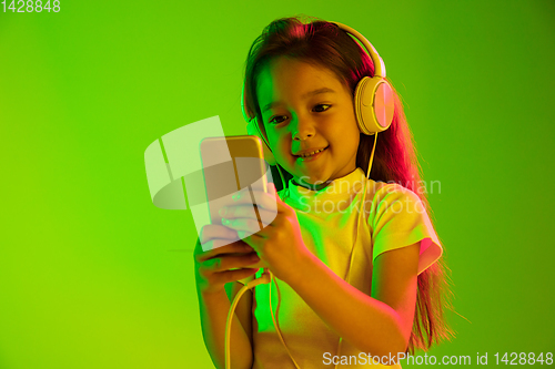 Image of Portrait of little girl in headphones on green background in neon light