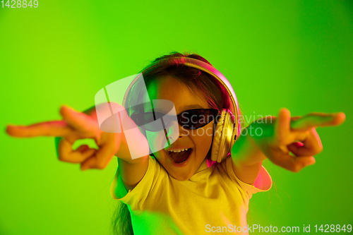 Image of Portrait of little girl in headphones on green background in neon light