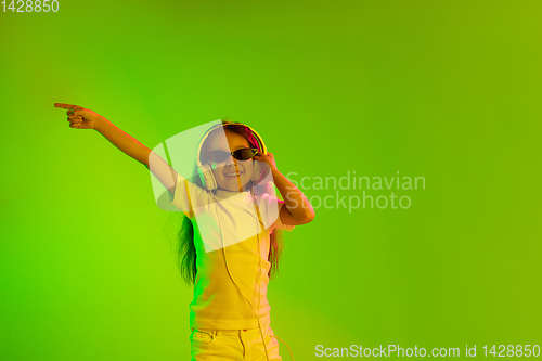 Image of Portrait of little girl in headphones on green background in neon light