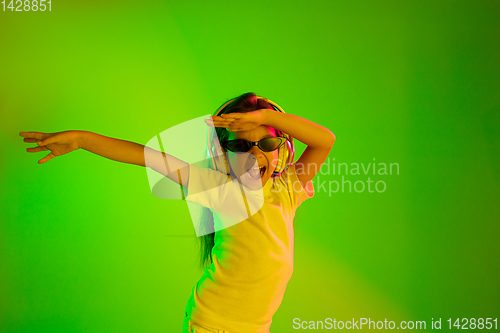 Image of Portrait of little girl in headphones on green background in neon light