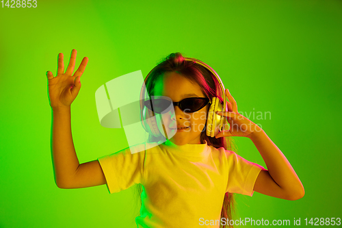 Image of Portrait of little girl in headphones on green background in neon light