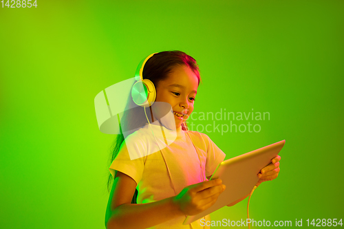 Image of Portrait of little girl in headphones on green background in neon light