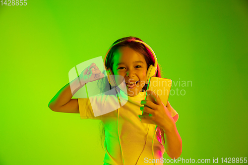 Image of Portrait of little girl in headphones on green background in neon light