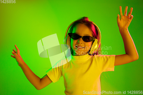 Image of Portrait of little girl in headphones on green background in neon light