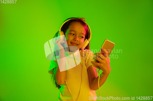 Image of Portrait of little girl in headphones on green background in neon light