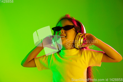 Image of Portrait of little girl in headphones on green background in neon light