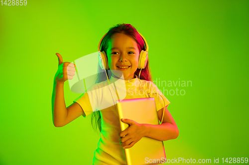 Image of Portrait of little girl in headphones on green background in neon light