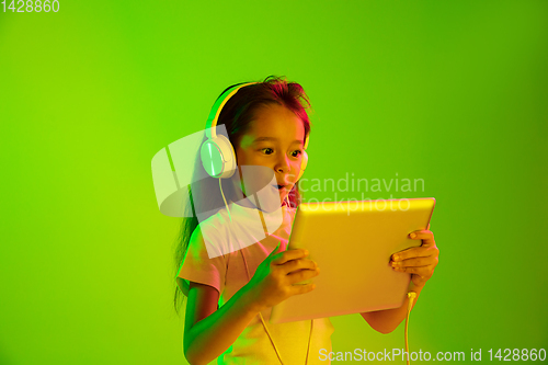 Image of Portrait of little girl in headphones on green background in neon light