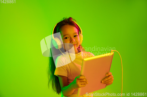 Image of Portrait of little girl in headphones on green background in neon light