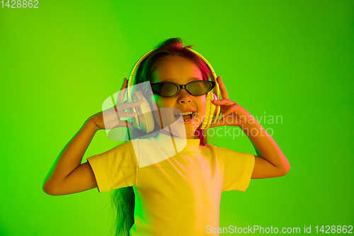 Image of Portrait of little girl in headphones on green background in neon light