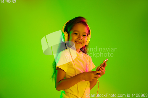 Image of Portrait of little girl in headphones on green background in neon light