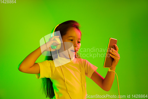 Image of Portrait of little girl in headphones on green background in neon light