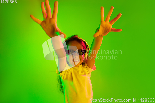 Image of Portrait of little girl in headphones on green background in neon light