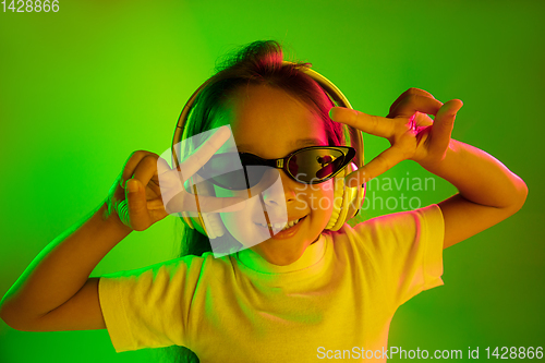 Image of Portrait of little girl in headphones on green background in neon light