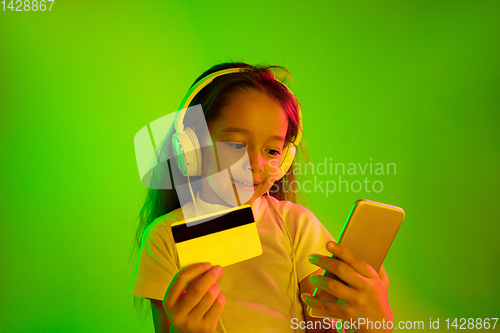 Image of Portrait of little girl in headphones on green background in neon light