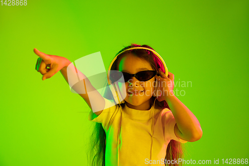 Image of Portrait of little girl in headphones on green background in neon light