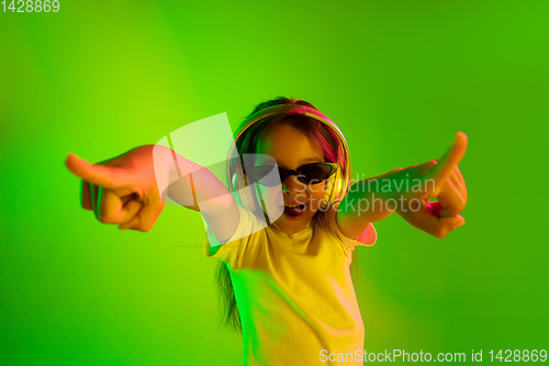 Image of Portrait of little girl in headphones on green background in neon light