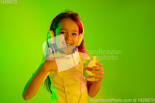 Image of Portrait of little girl in headphones on green background in neon light