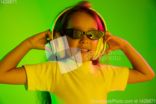 Image of Portrait of little girl in headphones on green background in neon light