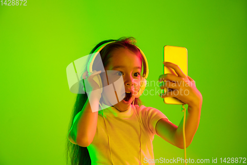 Image of Portrait of little girl in headphones on green background in neon light