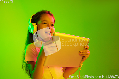 Image of Portrait of little girl in headphones on green background in neon light