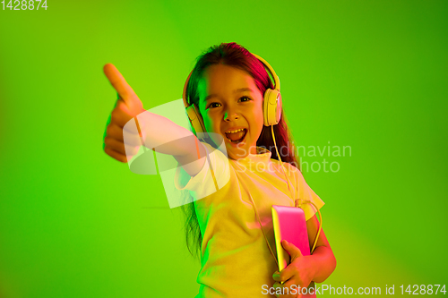 Image of Portrait of little girl in headphones on green background in neon light