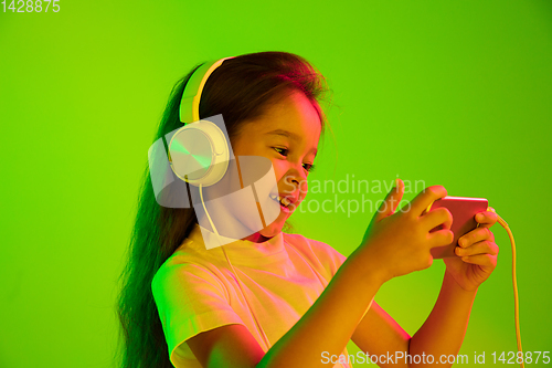 Image of Portrait of little girl in headphones on green background in neon light