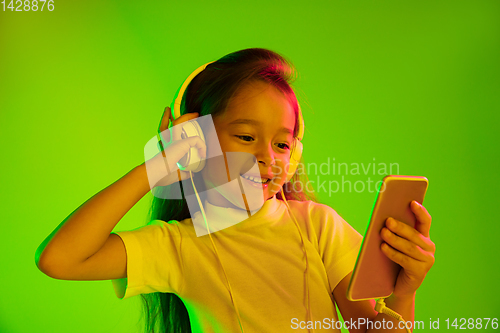 Image of Portrait of little girl in headphones on green background in neon light