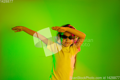 Image of Portrait of little girl in headphones on green background in neon light