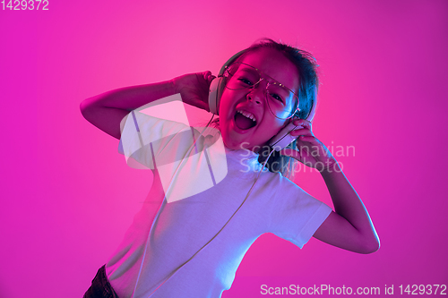 Image of Portrait of little girl in headphones on purple gradient background in neon light