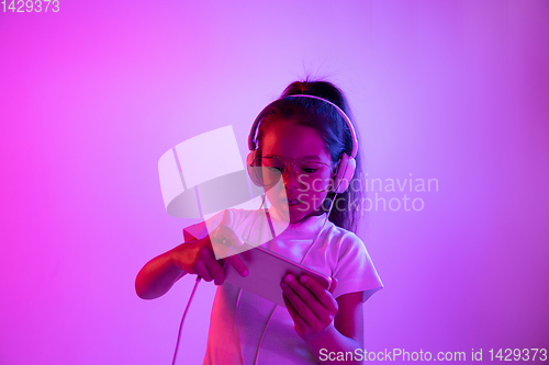 Image of Portrait of little girl in headphones on purple gradient background in neon light