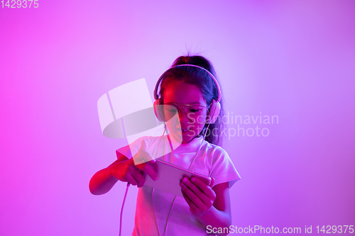 Image of Portrait of little girl in headphones on purple gradient background in neon light