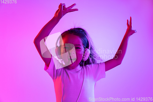 Image of Portrait of little girl in headphones on purple gradient background in neon light