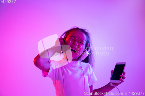 Image of Portrait of little girl in headphones on purple gradient background in neon light