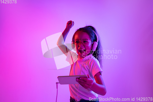 Image of Portrait of little girl in headphones on purple gradient background in neon light