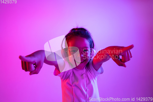 Image of Portrait of little girl in headphones on purple gradient background in neon light