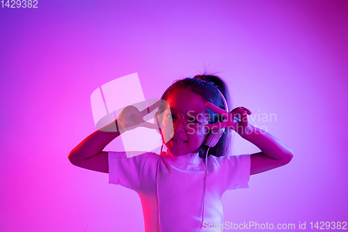 Image of Portrait of little girl in headphones on purple gradient background in neon light