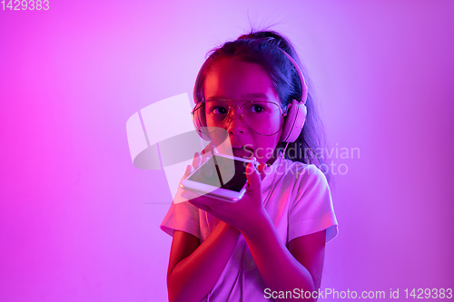 Image of Portrait of little girl in headphones on purple gradient background in neon light