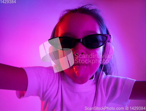 Image of Portrait of little girl in headphones on purple gradient background in neon light