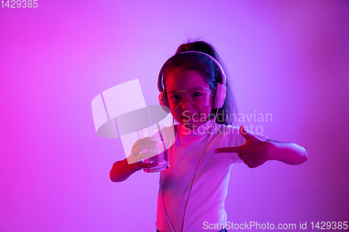 Image of Portrait of little girl in headphones on purple gradient background in neon light