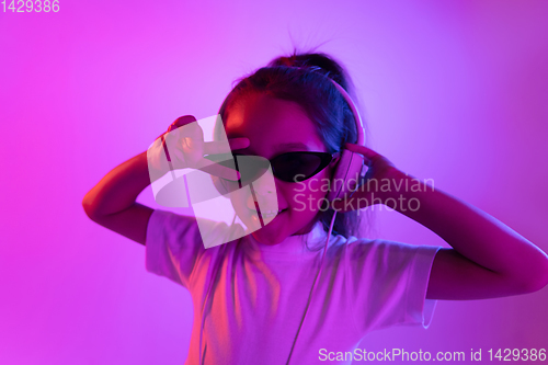 Image of Portrait of little girl in headphones on purple gradient background in neon light