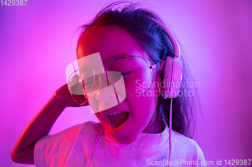 Image of Portrait of little girl in headphones on purple gradient background in neon light