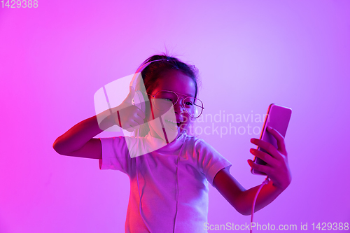 Image of Portrait of little girl in headphones on purple gradient background in neon light