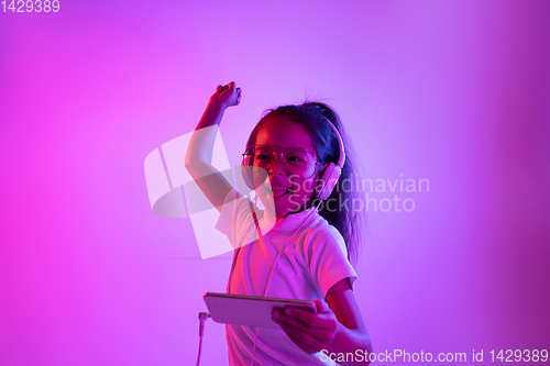 Image of Portrait of little girl in headphones on purple gradient background in neon light