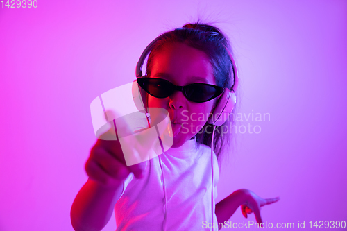 Image of Portrait of little girl in headphones on purple gradient background in neon light