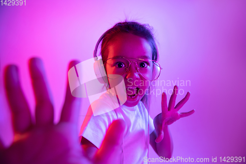 Image of Portrait of little girl in headphones on purple gradient background in neon light