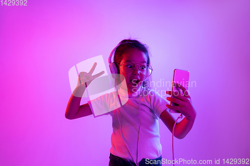 Image of Portrait of little girl in headphones on purple gradient background in neon light