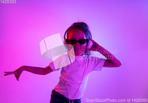 Image of Portrait of little girl in headphones on purple gradient background in neon light